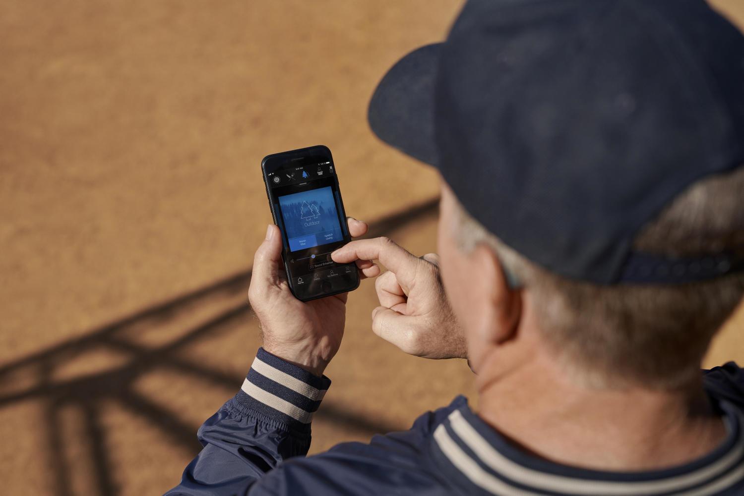 Coach wearing Beltone Amaze rechargeble hearing aids use Beltone Remote Care through HearMax app on smartphone.