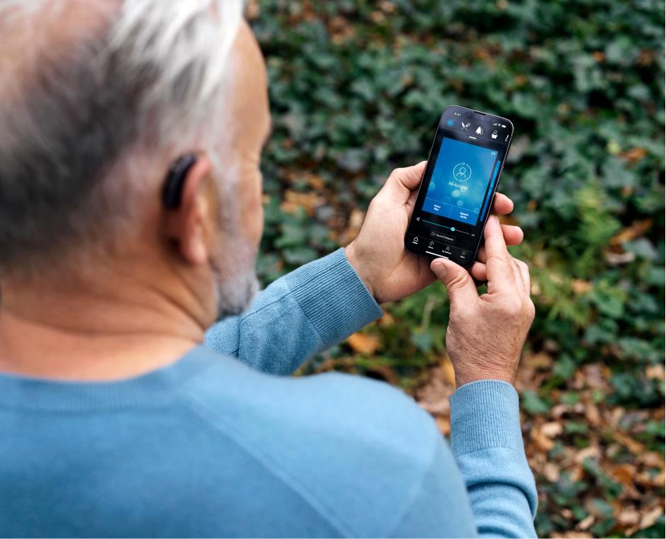 Man with BTE hearing aids using the Beltone HearMax app on his smartphone