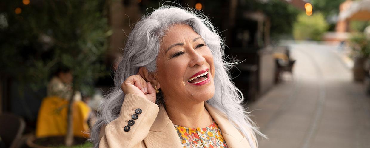 Mujer sonriente pulsando un botón en su audífono ReSound