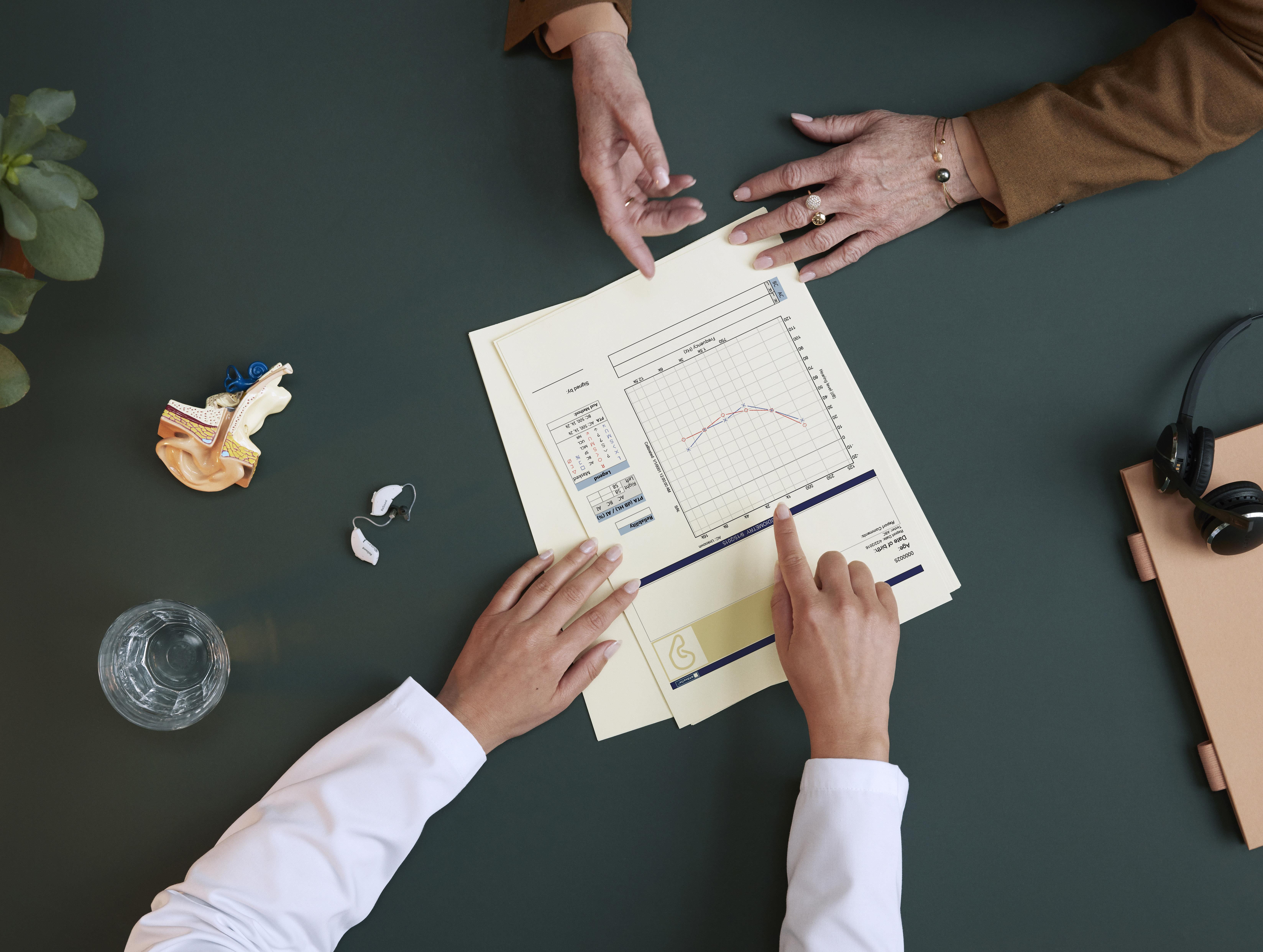 Profissional de cuidados auditivos que aconselha um paciente e mostra um audiograma.