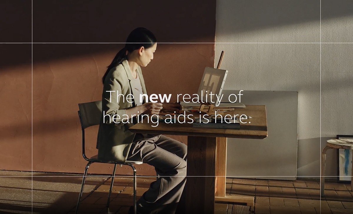 Woman seated indoors with text overlay reading A new reality of hearing aids is here