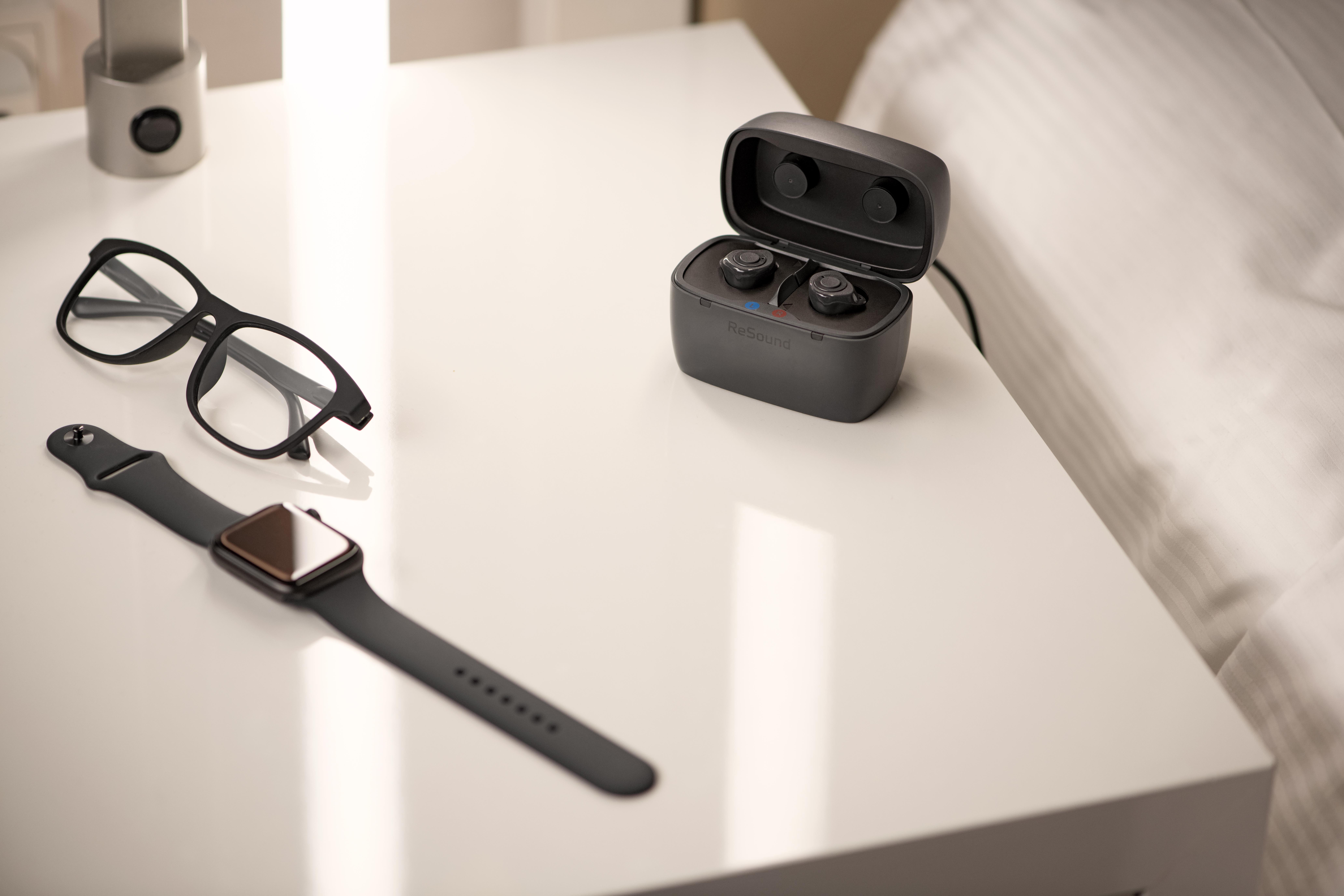 Customs by ReSound on charger beside with glasses and watch